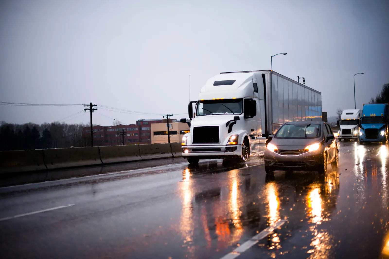A commercial truck and passenger vehicle travelling on a wet road.